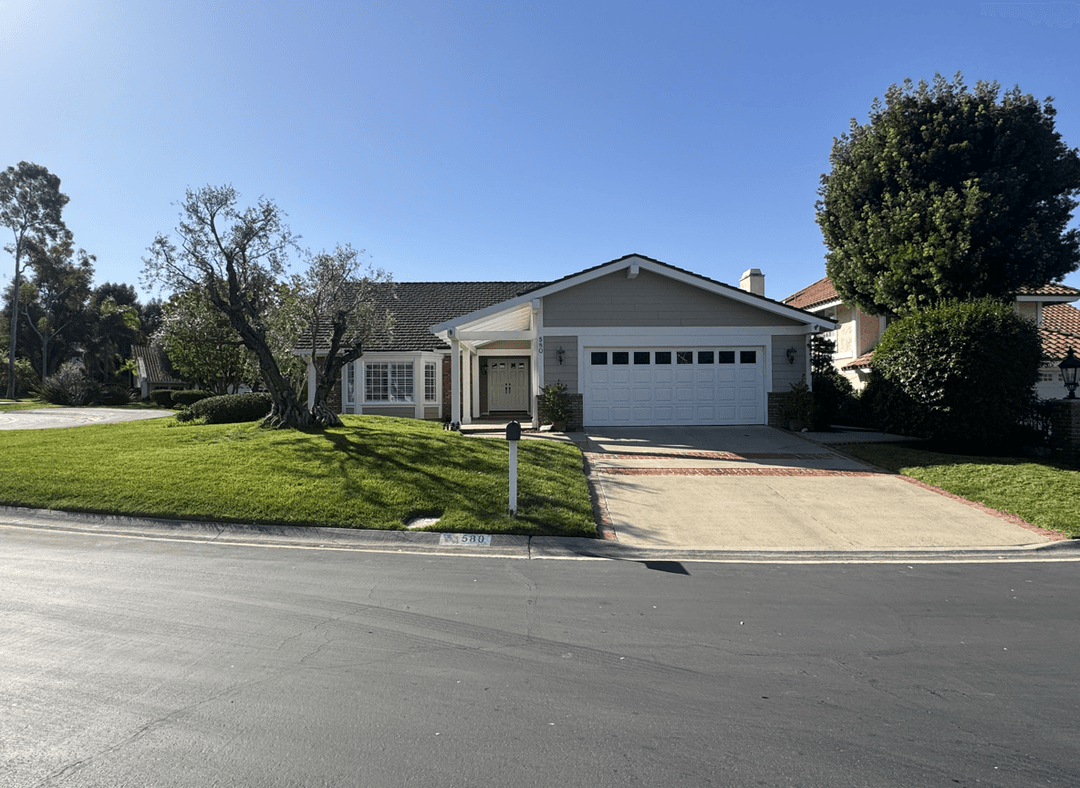 Front view of a house with driveway, grass, and plants.