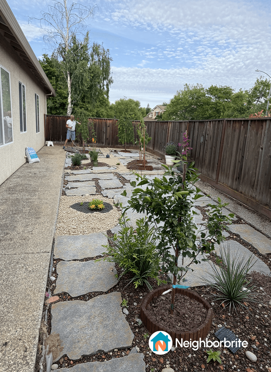 A yard with stone pathways, plants, and a person watering.