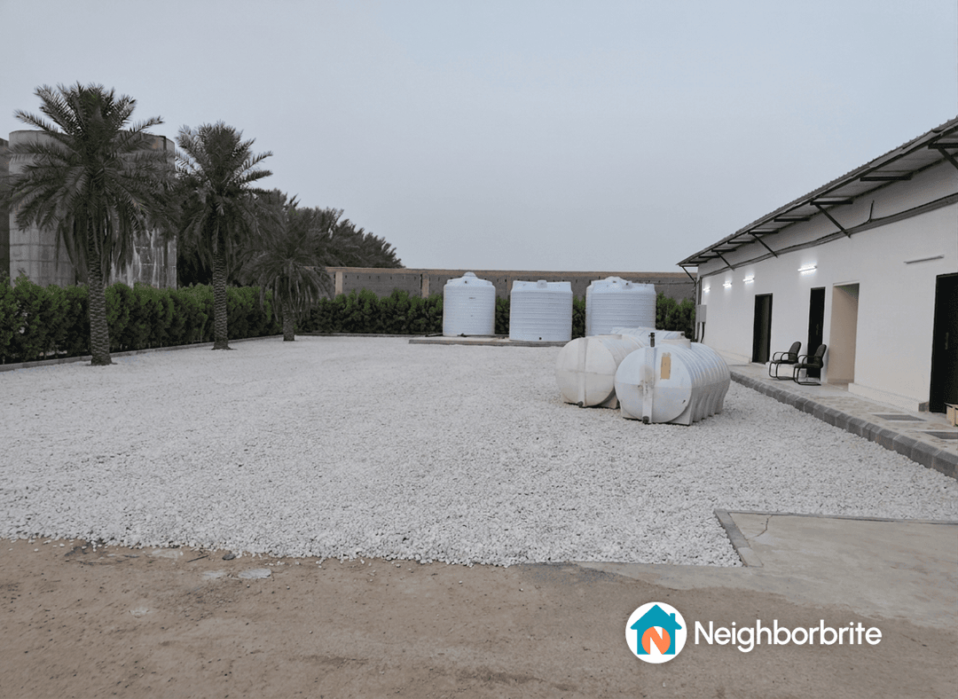 A yard with white gravel and water tanks, showing a concrete slab area.
