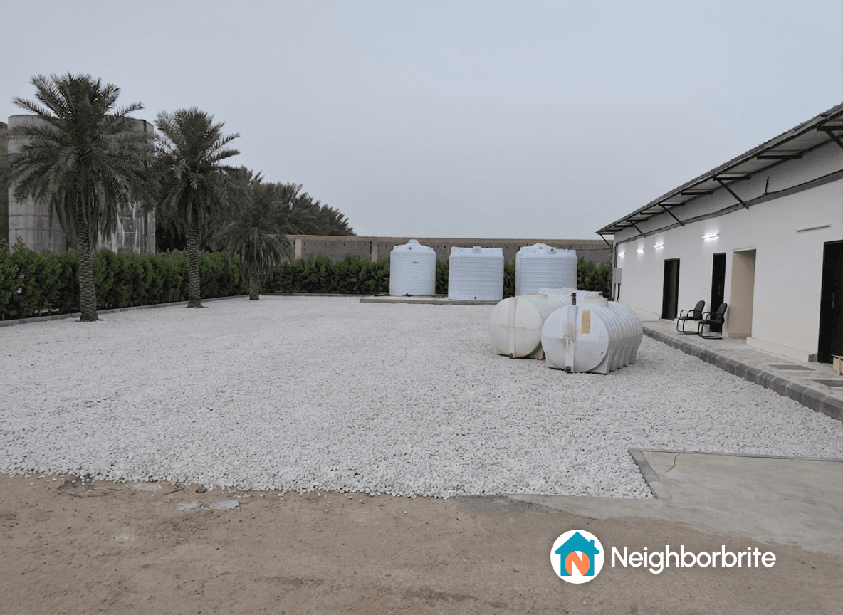 A yard with white gravel and water tanks, showing a concrete slab area.