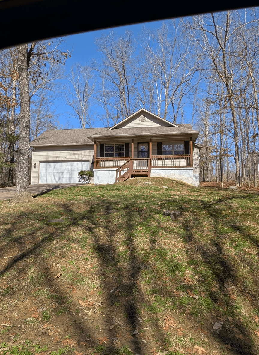 Front view of a house with a sloped yard and trees in the background.