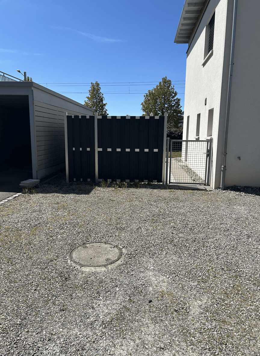 A garden area with a fence and gravel surface, ready for container placement.