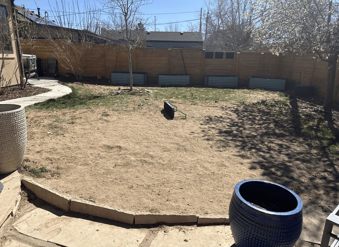 A yard with damaged grass, featuring a patio area and planters.