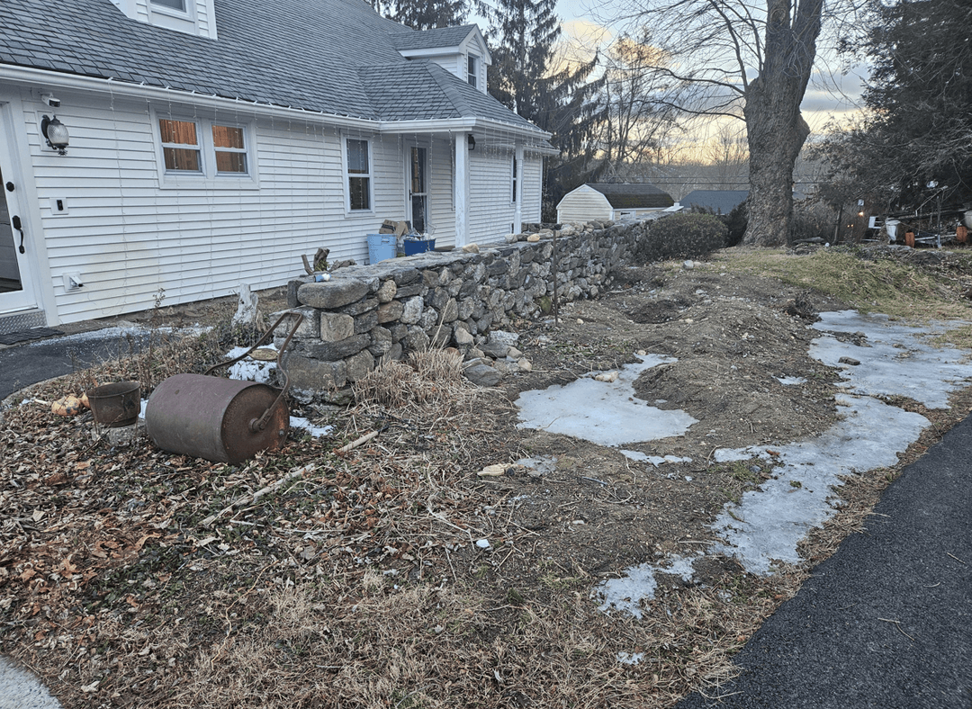 A yard with a stone wall, some debris, and patches of ice.