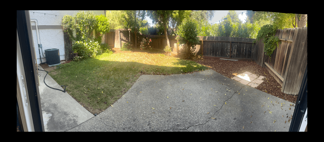 View of a backyard with grass, concrete, and wooden fence, seeking design ideas for pavers and a pergola.