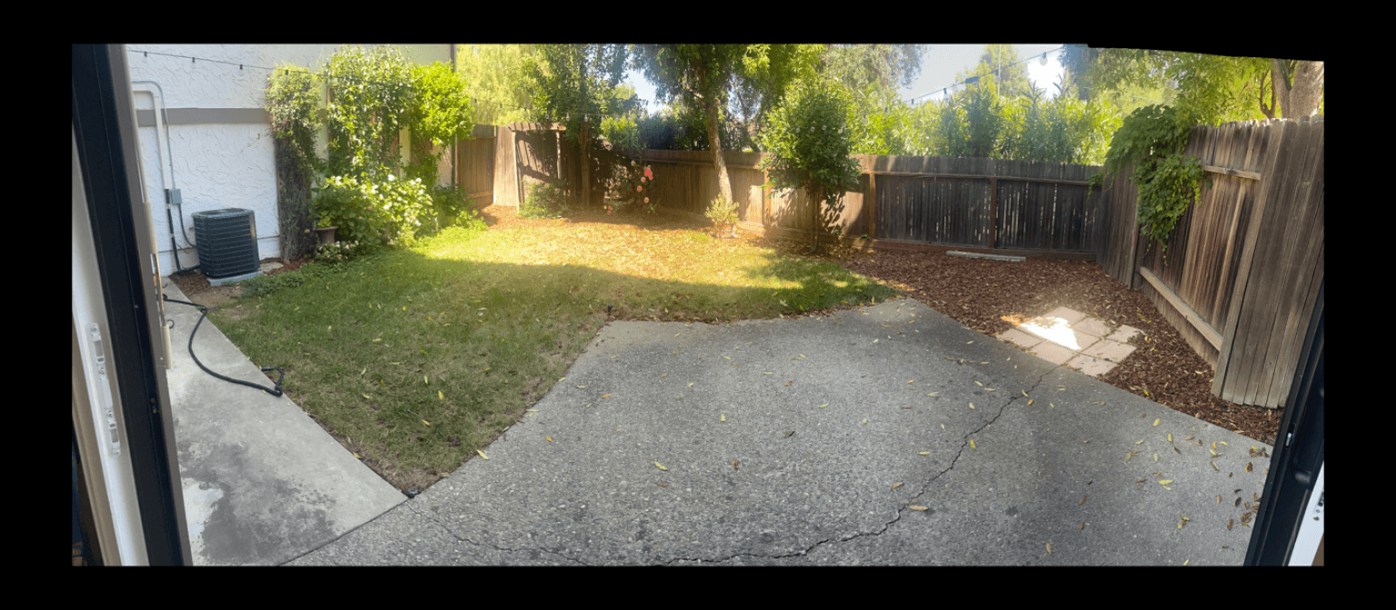View of a backyard with grass, concrete, and wooden fence, seeking design ideas for pavers and a pergola.