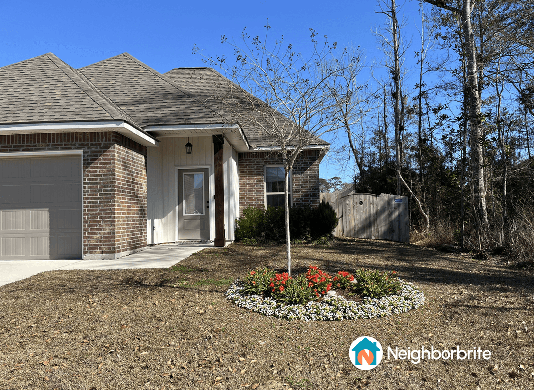 A front yard with a flower bed featuring colorful blooms and a small tree.