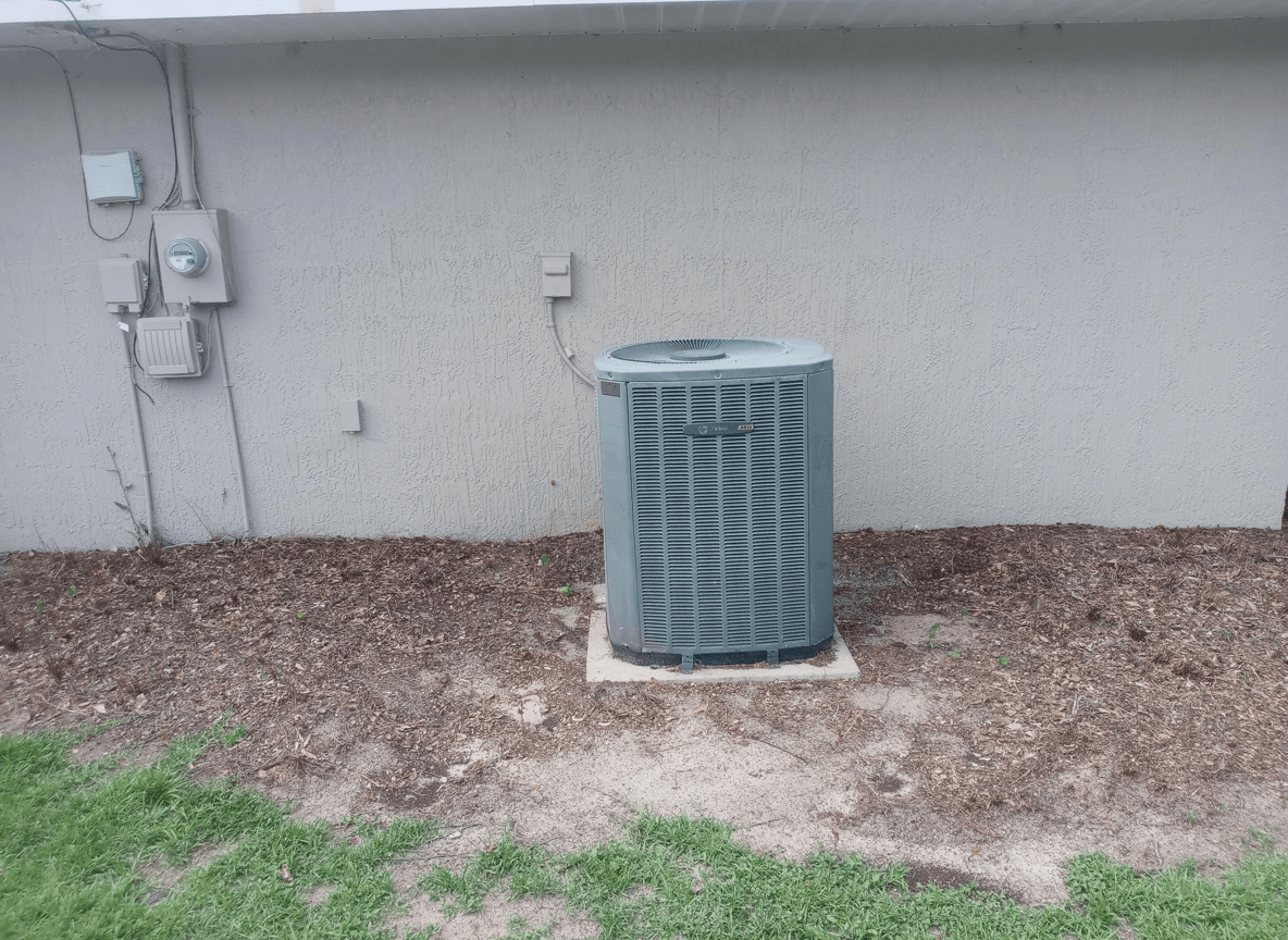 Air conditioning unit in a yard with bare soil and grass.