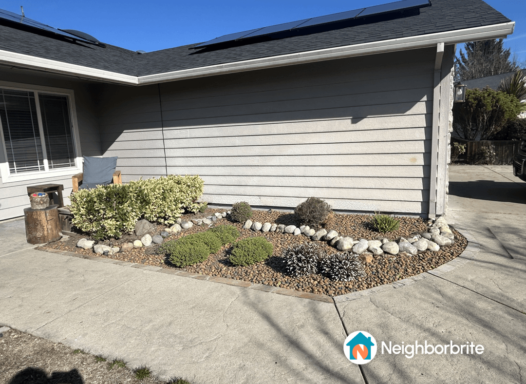 A landscaped yard with rocks, plants, and a seating area.