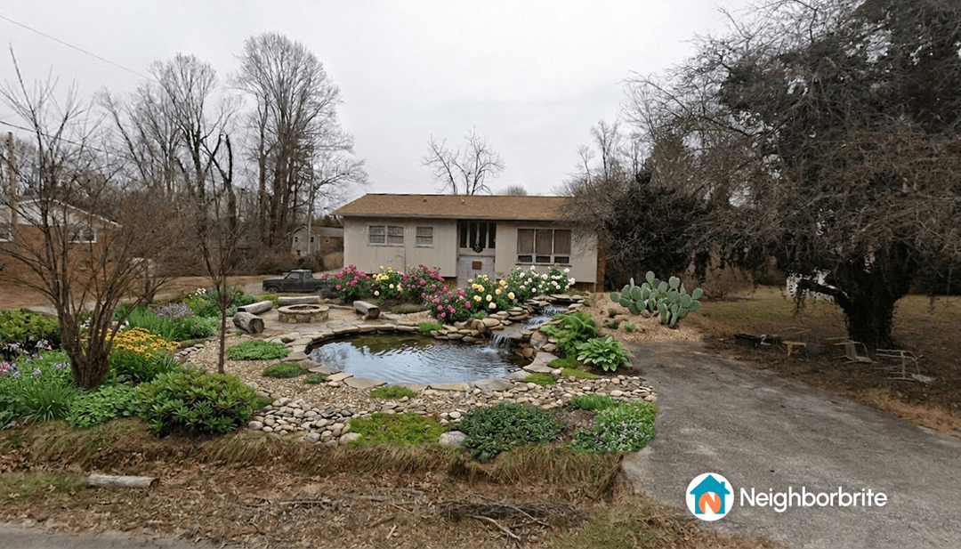 A yard featuring a pond, flowers, cacti, and a fire pit area.