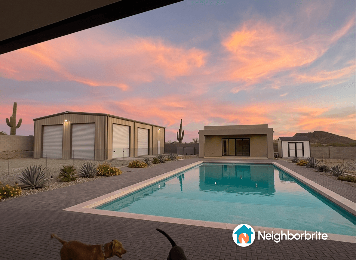 View of a backyard with a pool, garage, and retaining wall at sunset.
