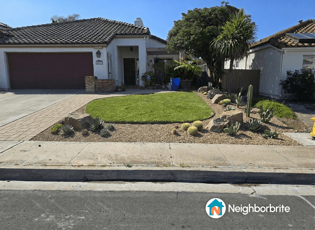 A landscaped front yard featuring grass, rocks, and various plants.