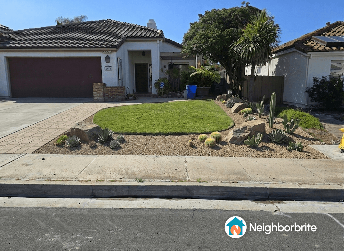 A landscaped front yard featuring grass, rocks, and various plants.