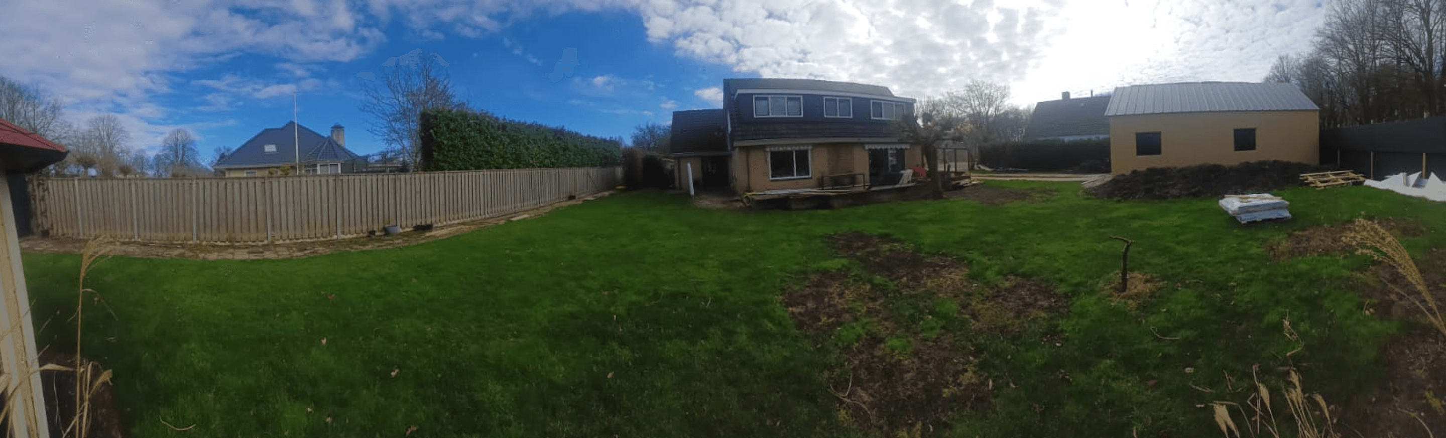 Panorama van een tuin met terras, looppad en grasveld.