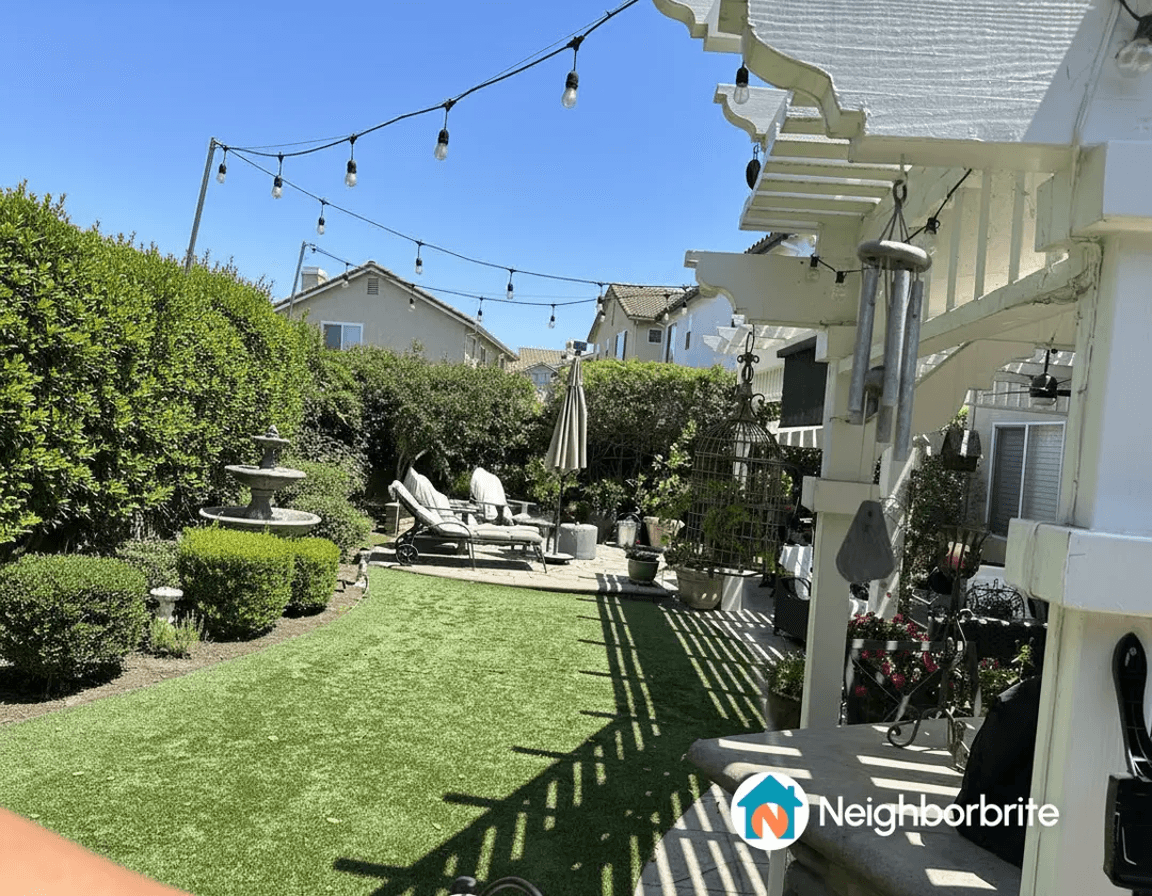 A landscaped yard featuring a fountain, lounge chairs, and covered patio with decorative elements.