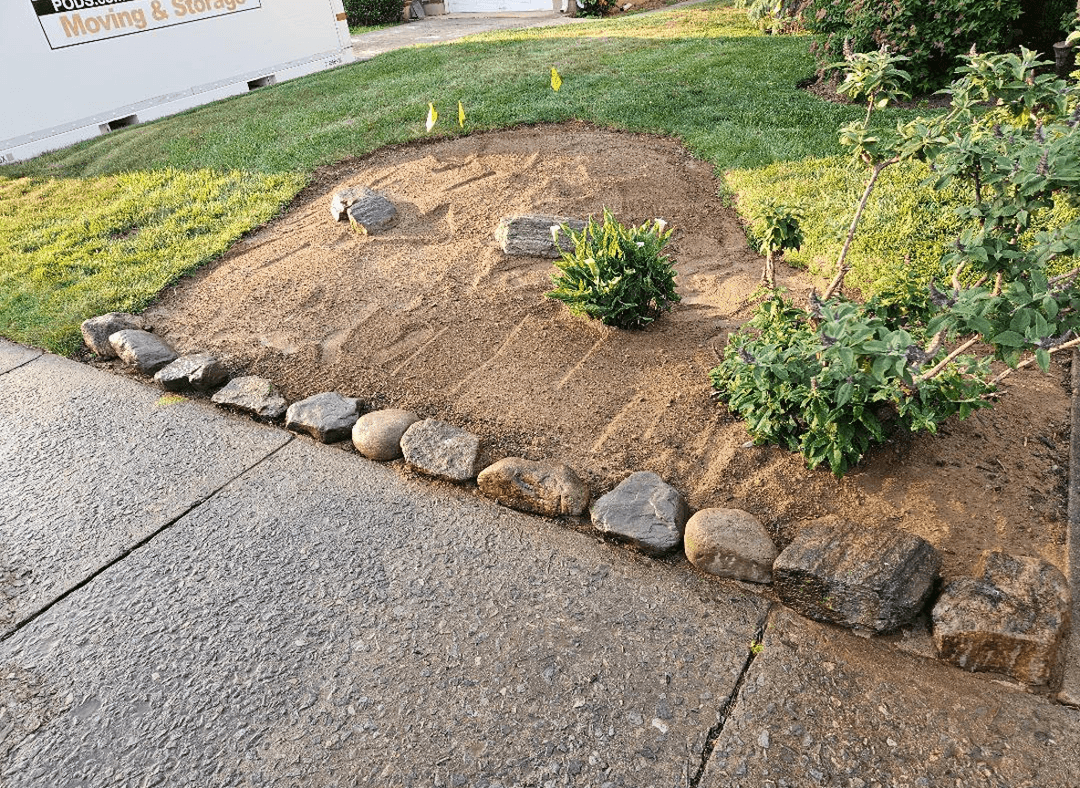 A garden area with rocks bordering a sidewalk, preparing for perennial planting.