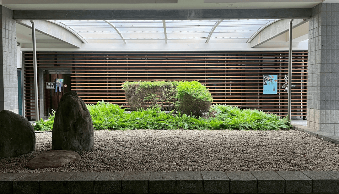 A modern landscape featuring greenery, rocks, and wooden slats in a semi-outdoor space.