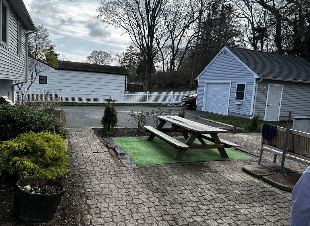 A patio area with a picnic table, driveway, and landscaping.