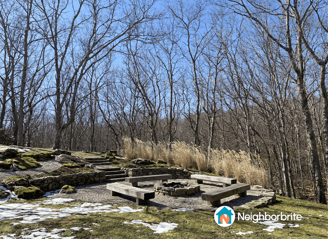 A yard with stone steps, retaining wall, and fire pit area, surrounded by trees and grass.