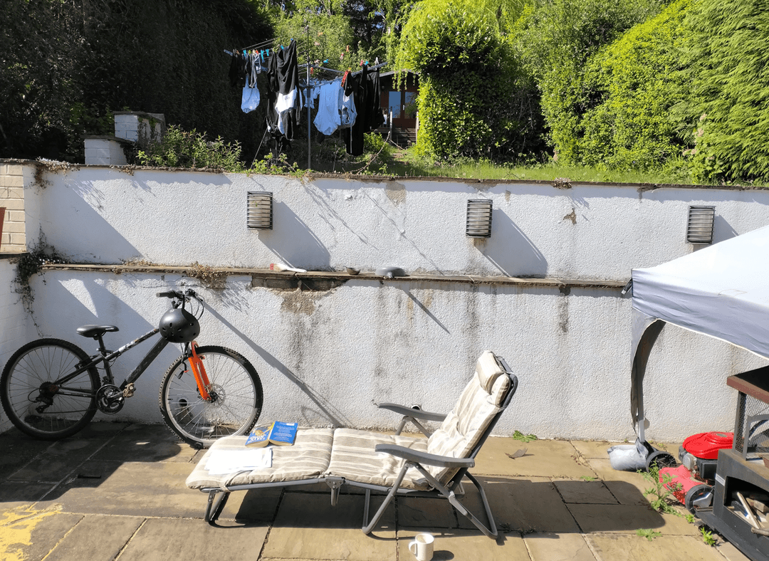 A backyard scene with a retaining wall, bicycle, and laundry hanging.