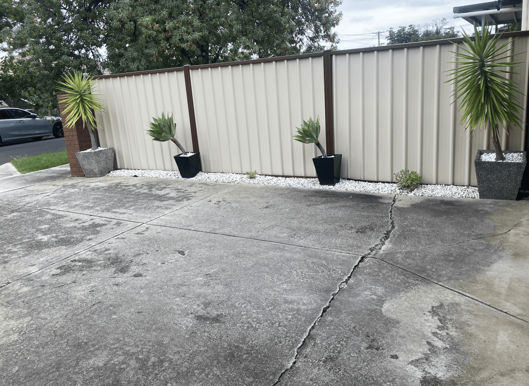 A concrete driveway with potted plants and a fence.