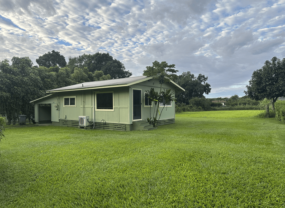 A green house surrounded by lush grass and trees under a cloudy sky.