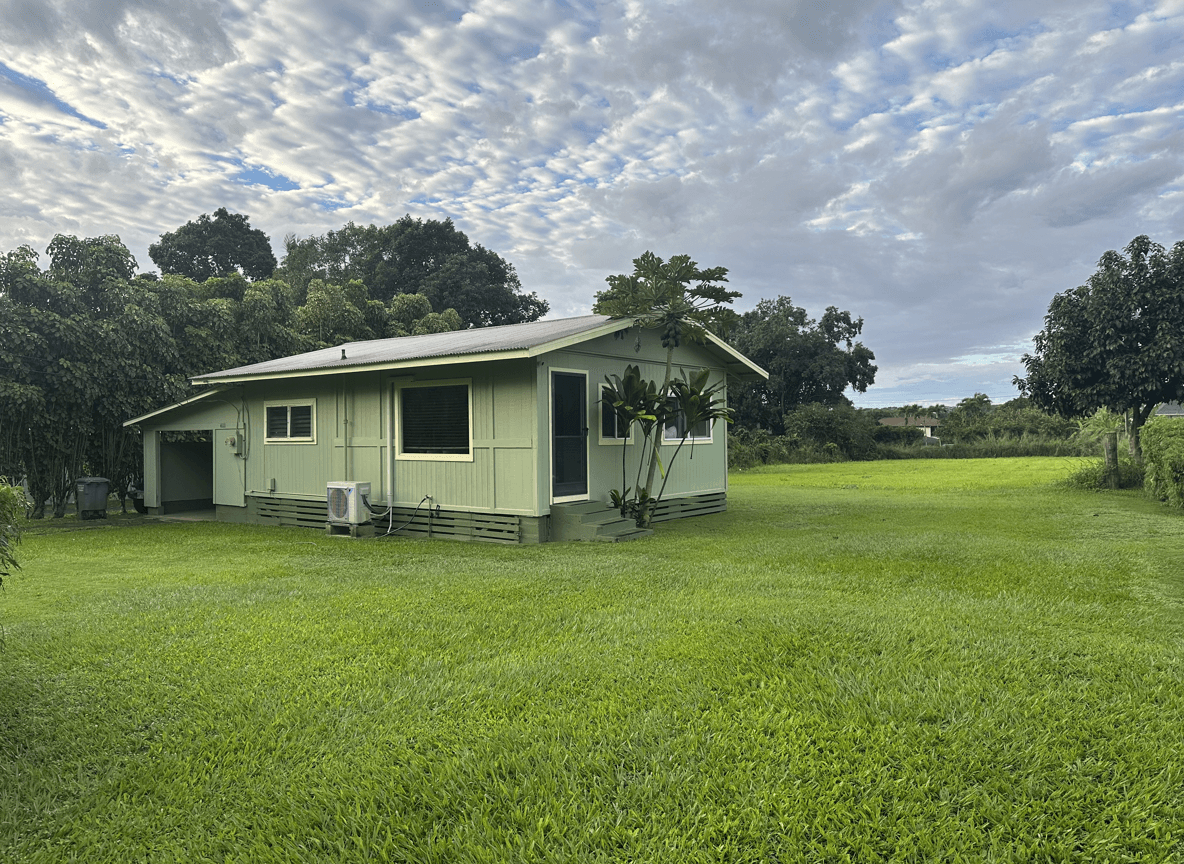 A green house surrounded by lush grass and trees under a cloudy sky.