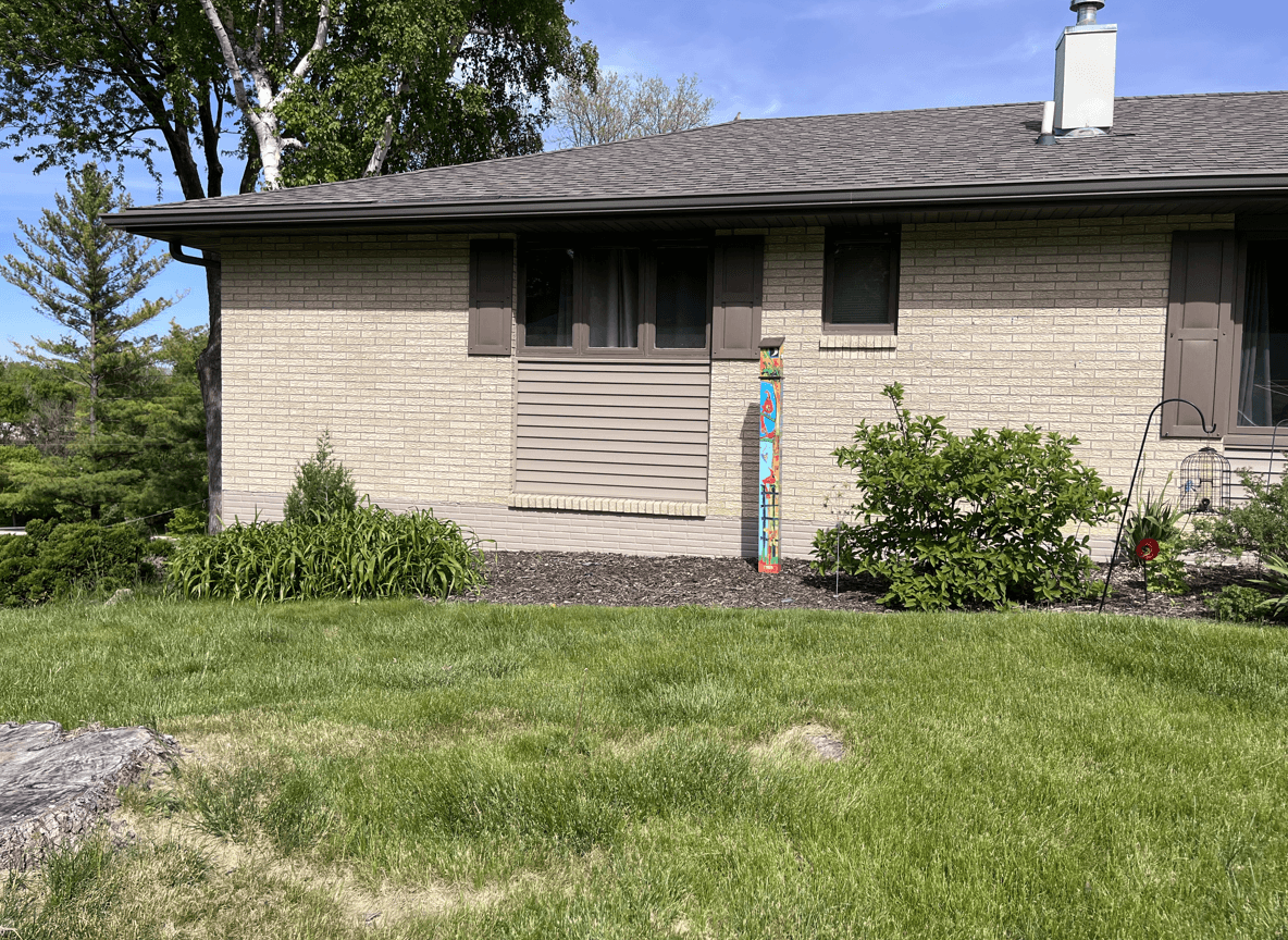 A house with landscaping, featuring a colorful totem and greenery.