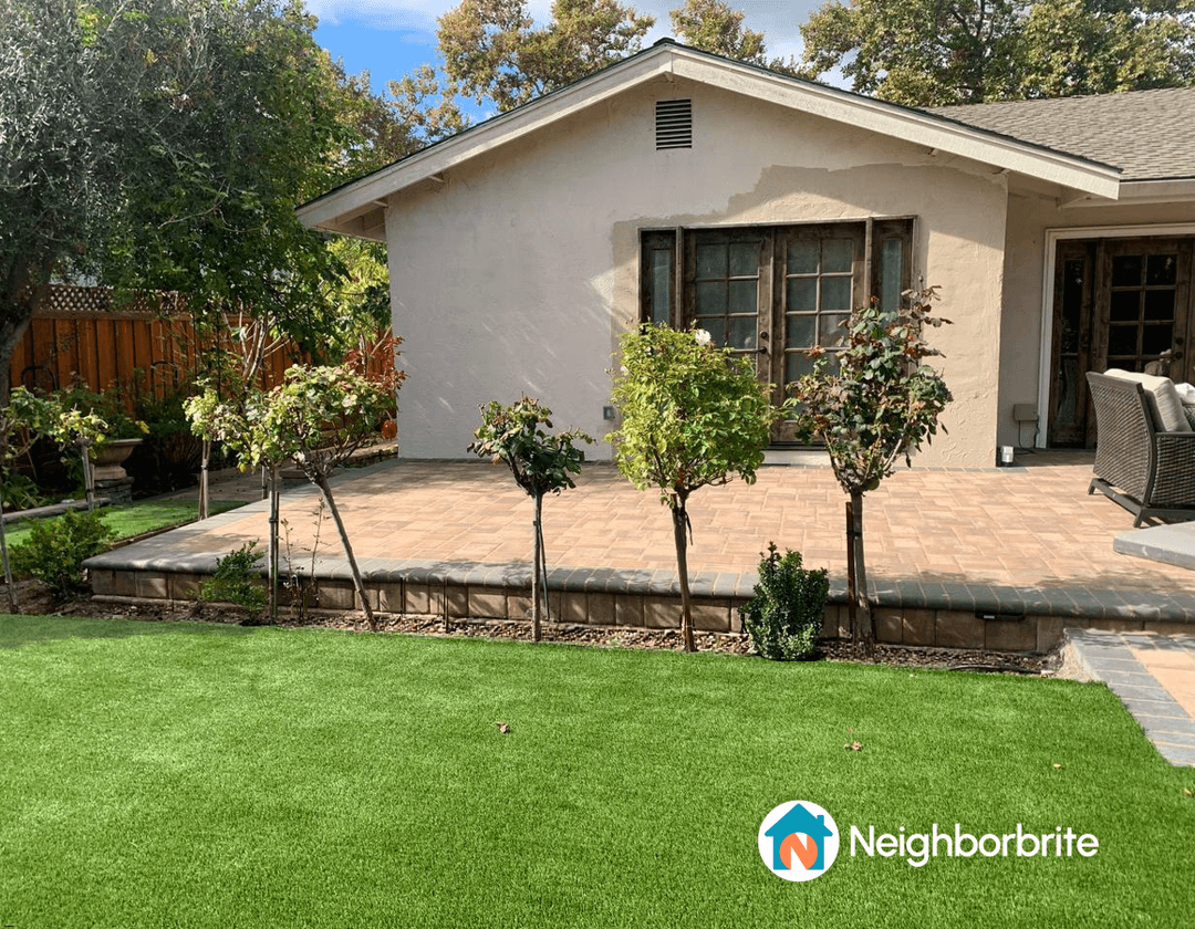 A house with white walls and a black roof, surrounded by greenery.