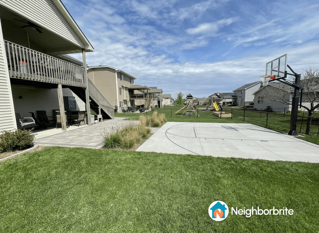 A backyard with a concrete basketball court and patio area.