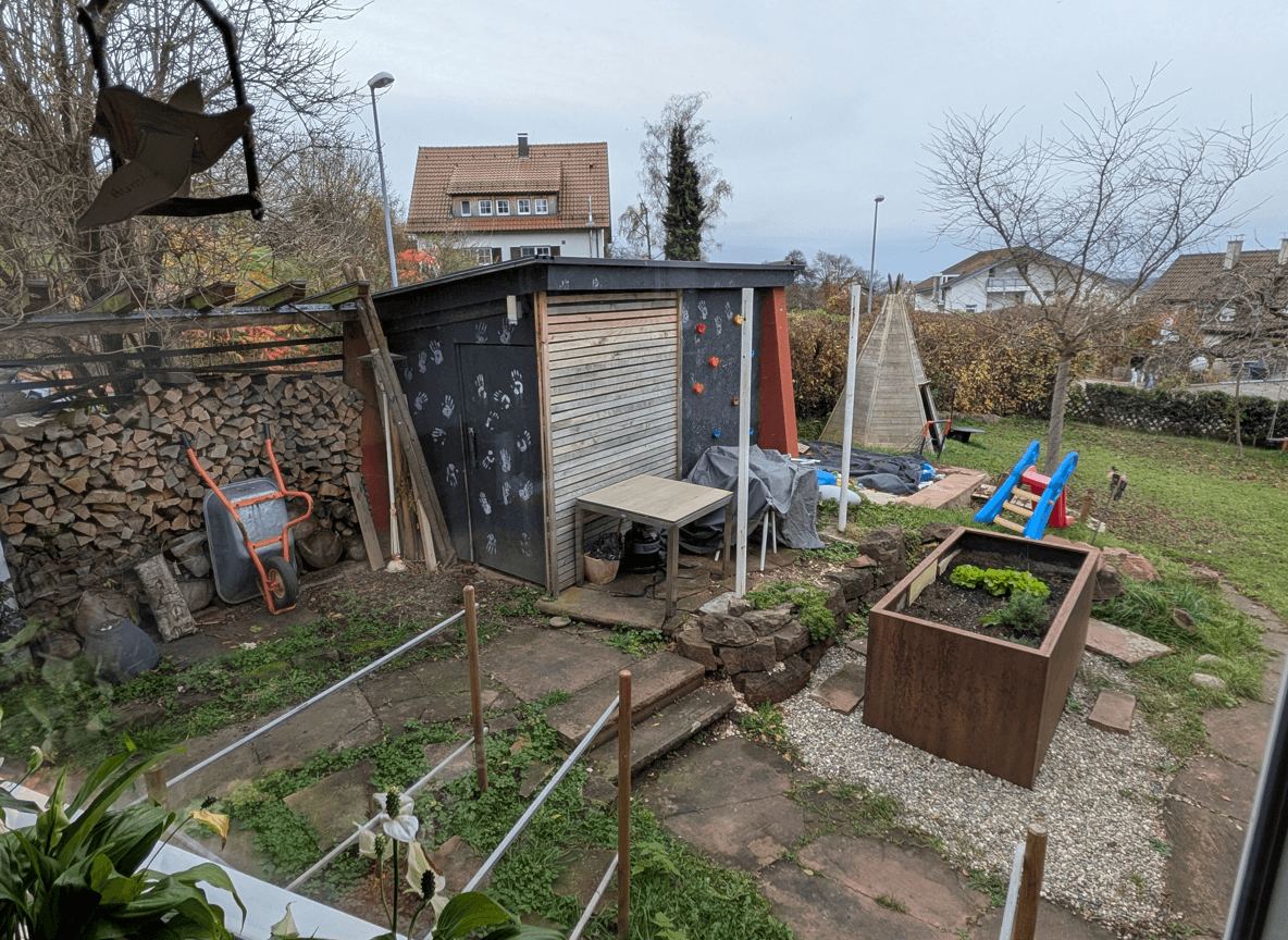A cluttered yard area with a shed, climbing wall, and garden bed.