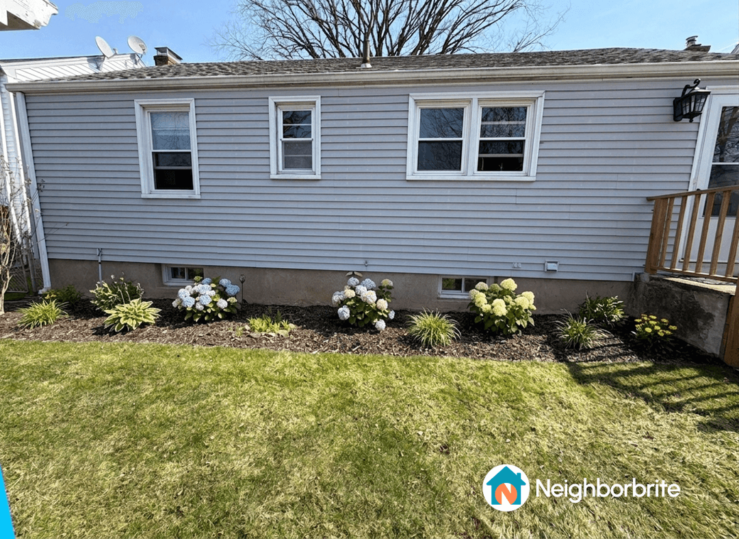 A garden bed featuring coral bells and sedum plants near a house.