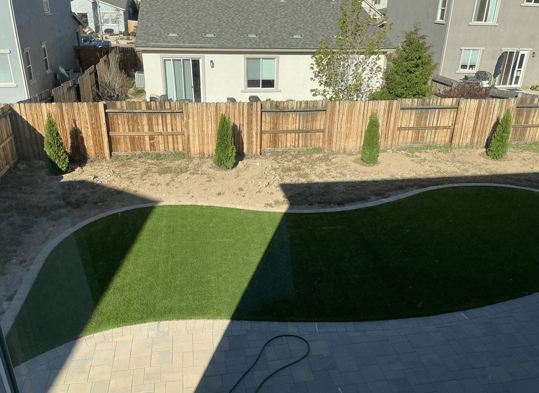 View of a backyard with artificial grass and small trees.