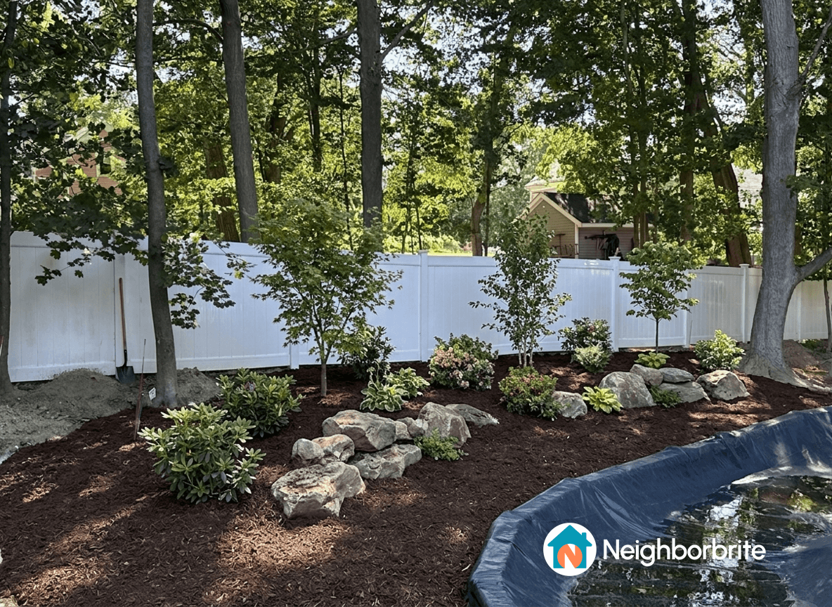 A landscaped yard with plants, rocks, and a fence, ready for speakers.