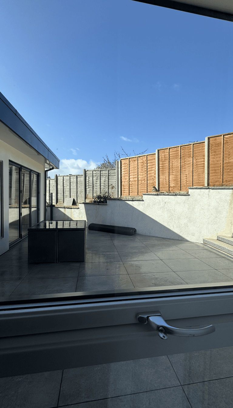 View from a window showing a patio area with a fence and some plants.