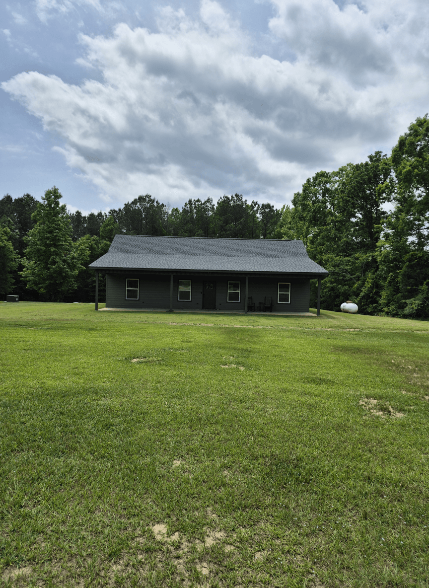 A house surrounded by a large grassy yard and trees in the background.