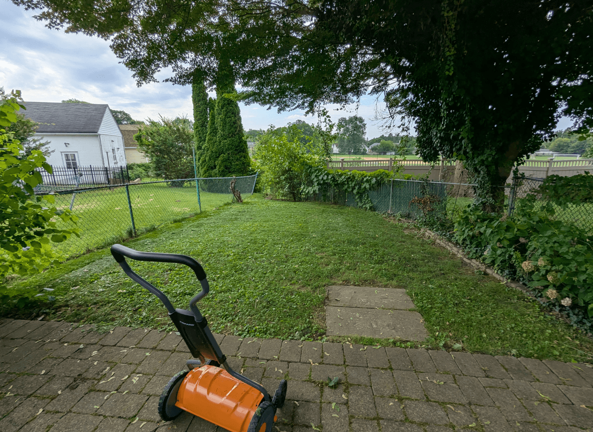 A backyard with a lawn and a garden area, featuring a gardening tool.
