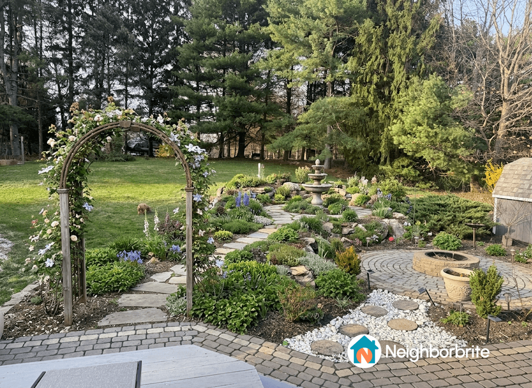 A small bucket fountain surrounded by vibrant flowers and greenery in a landscaped garden.