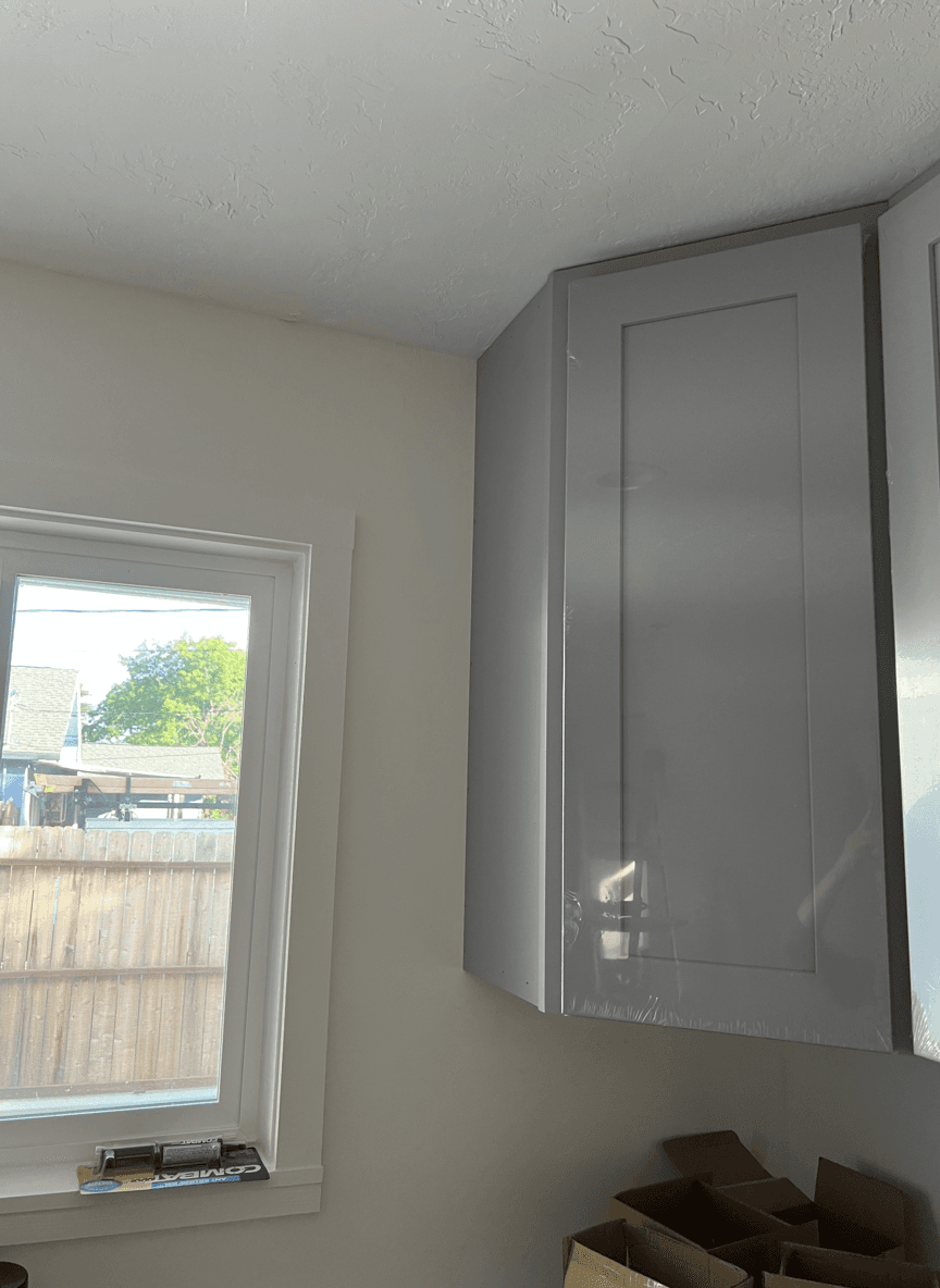 A corner next to kitchen cabinets and a window, showing space for a shelf.