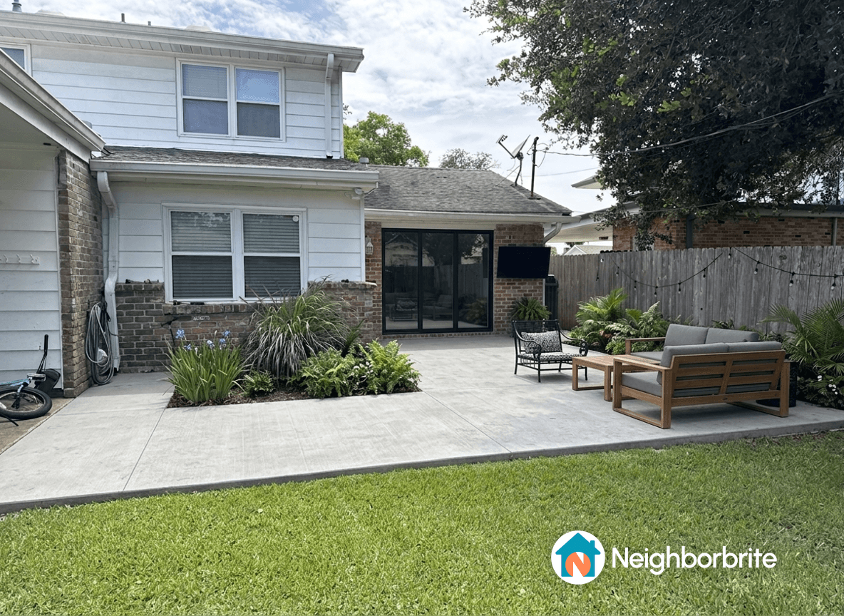 A backyard with a concrete area, seating, and plants along the fence.