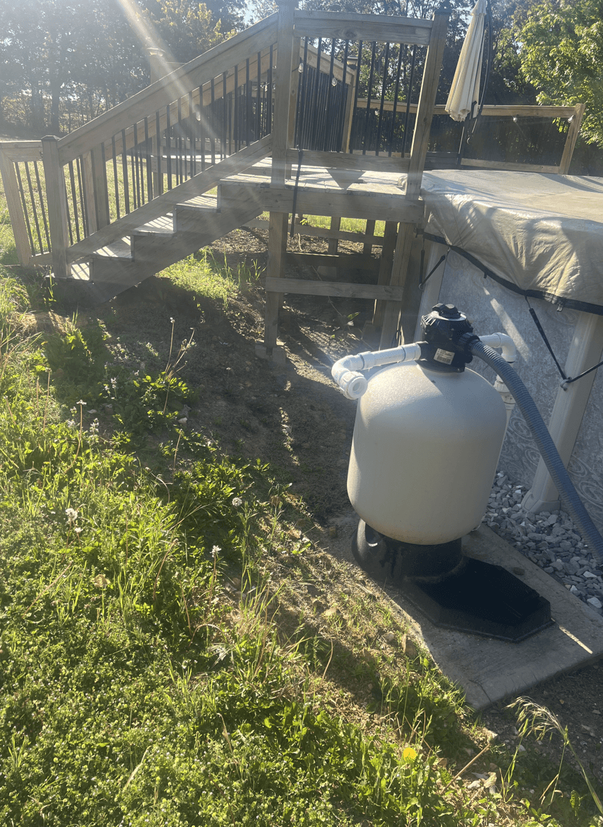 A backyard with stairs, a sand filter, and overgrown grass.