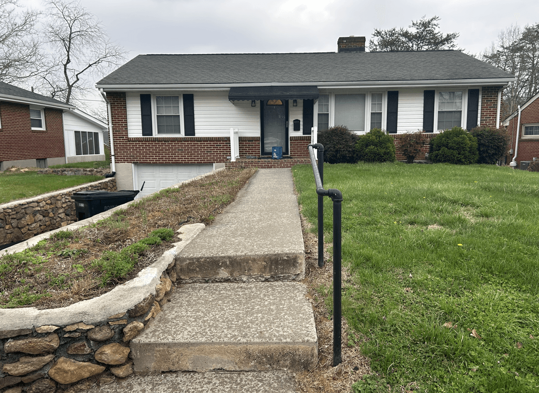 A concrete sidewalk leading to a house, with grass and bushes around.
