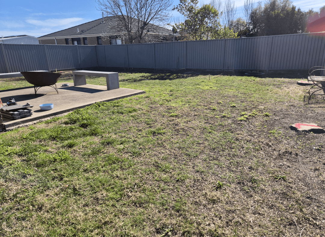 A backyard with a concrete area, a fire pit, and grass, looking for landscaping ideas.