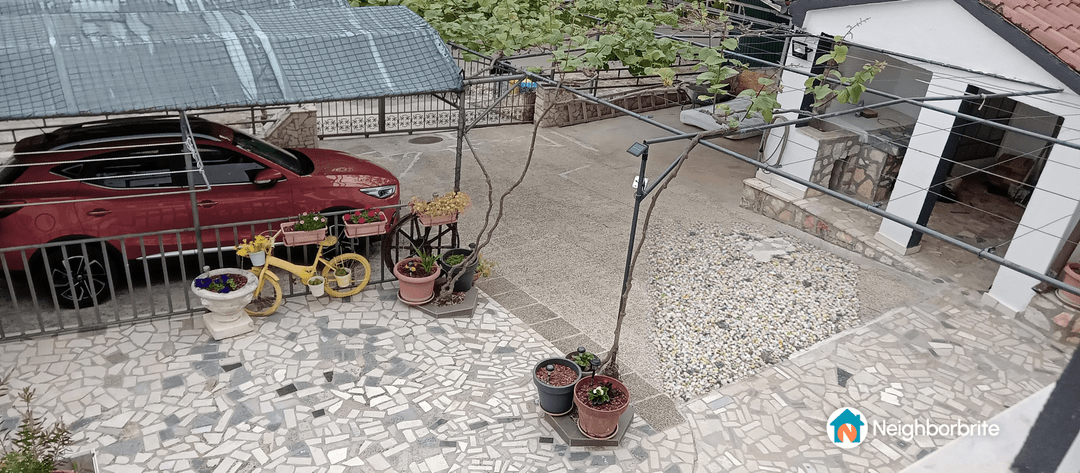 A view of a landscaped yard with a red car, potted plants, and a decorative yellow bicycle.