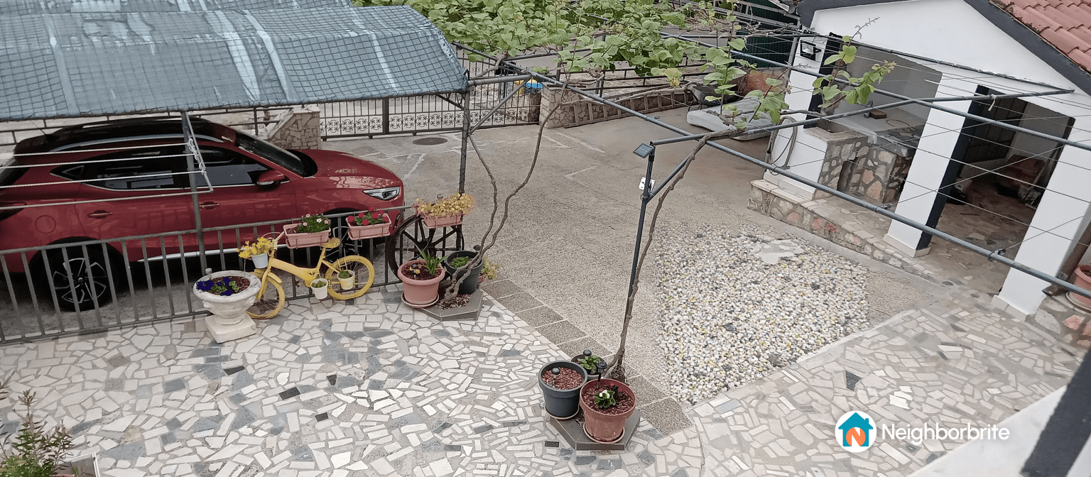 A view of a landscaped yard with a red car, potted plants, and a decorative yellow bicycle.