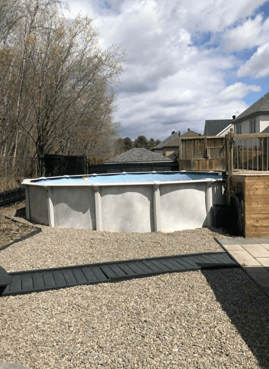 A backyard scene featuring a pool area with gravel, trees, and a wooden deck.
