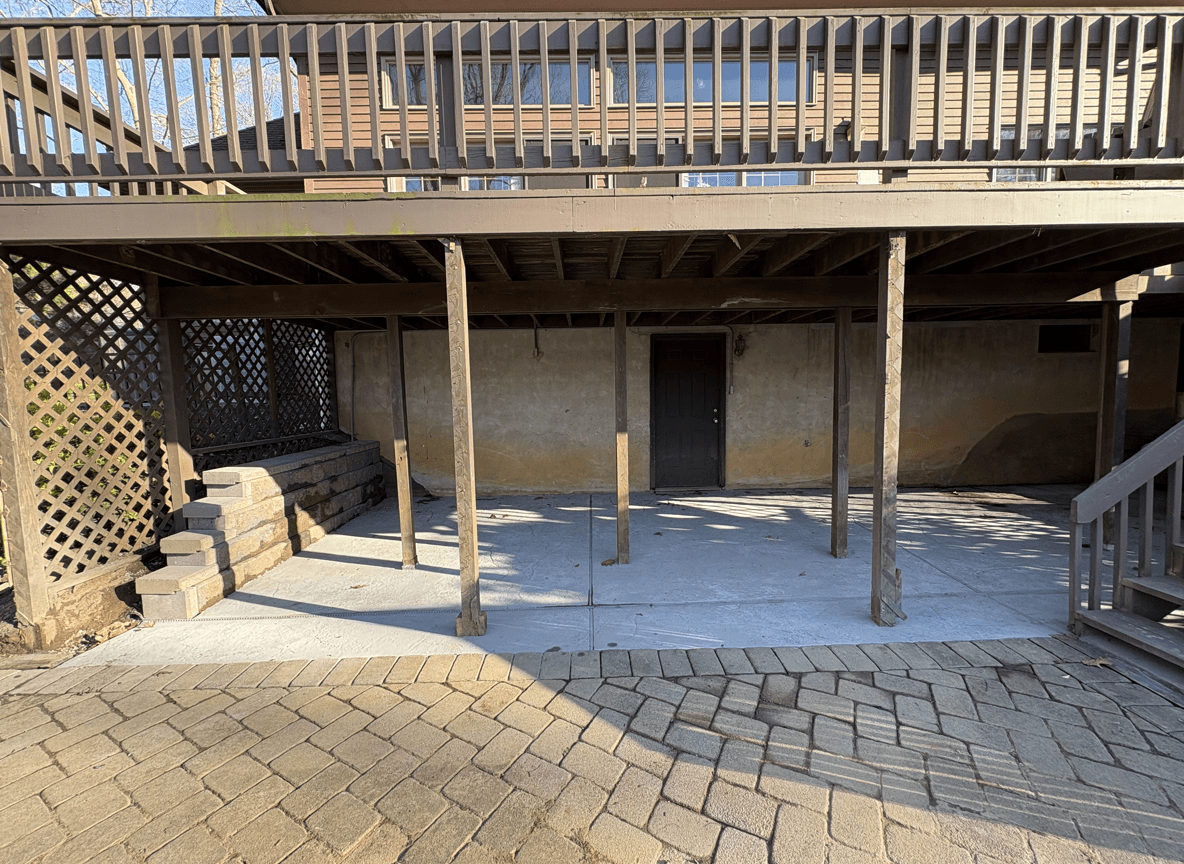 An empty under-deck area with concrete floor and stone steps.