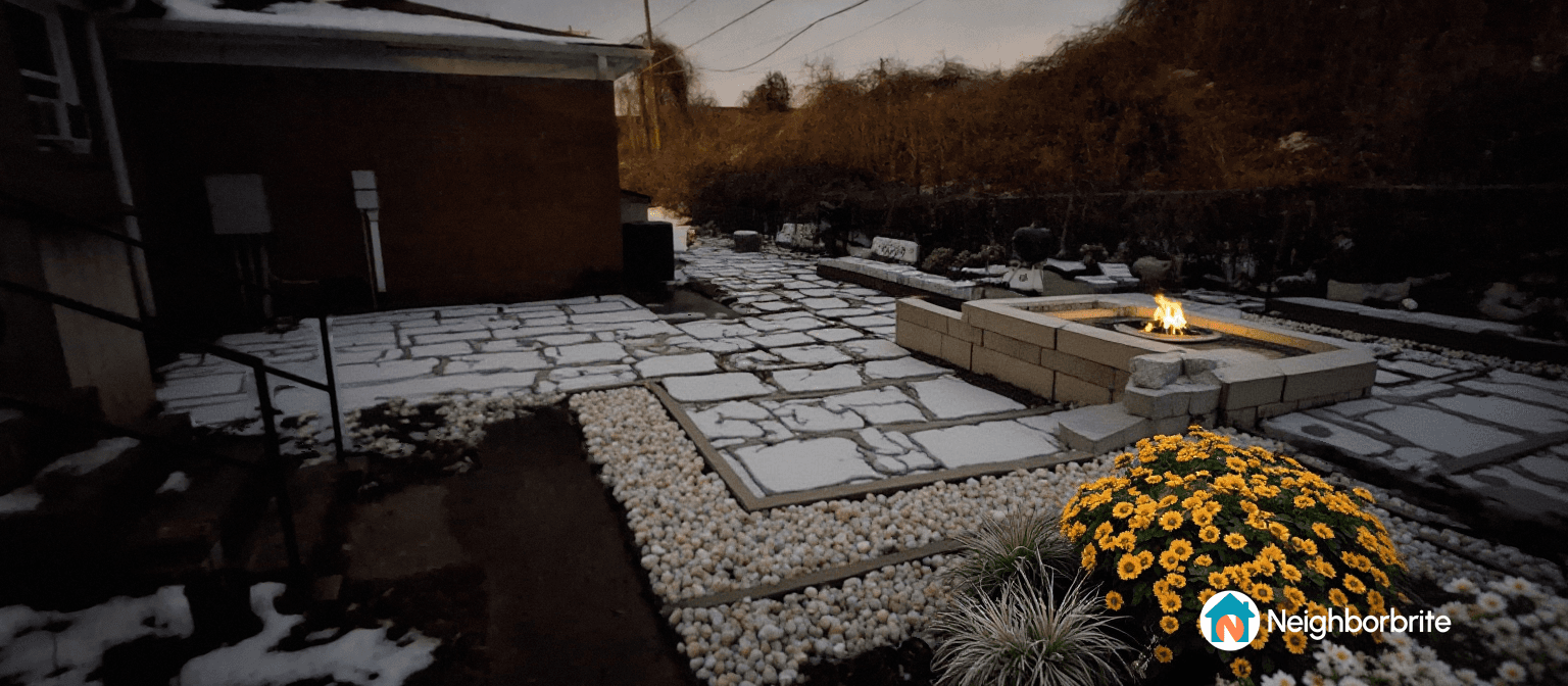 A cozy outdoor area featuring a fire pit, stone pathway, and flowers, illuminated at dusk.