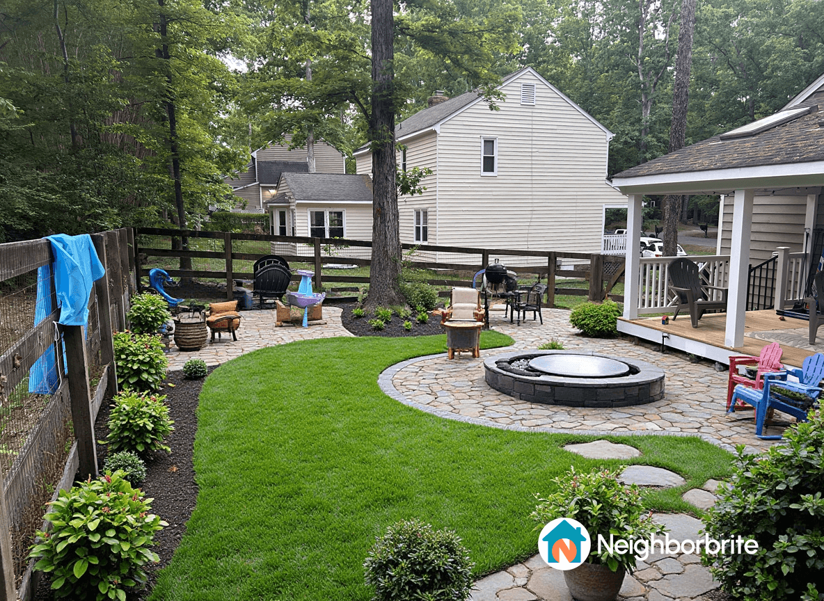A backyard featuring grass, a fire pit, and stone areas.