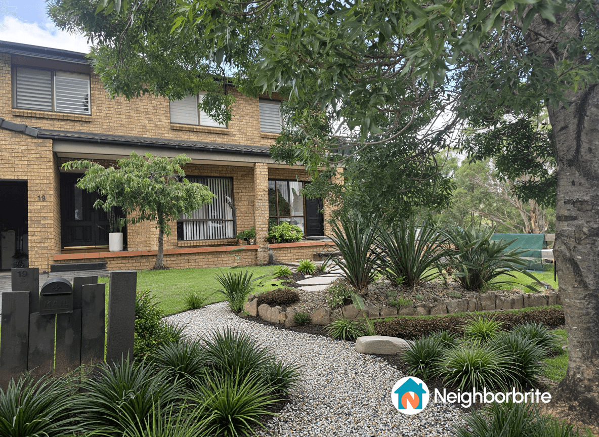 A landscaped yard with plants, gravel paths, and a brick house.